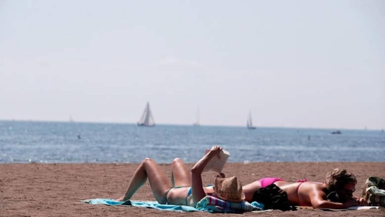 Deux femmes en bikini lisent, étendues sur la plage.