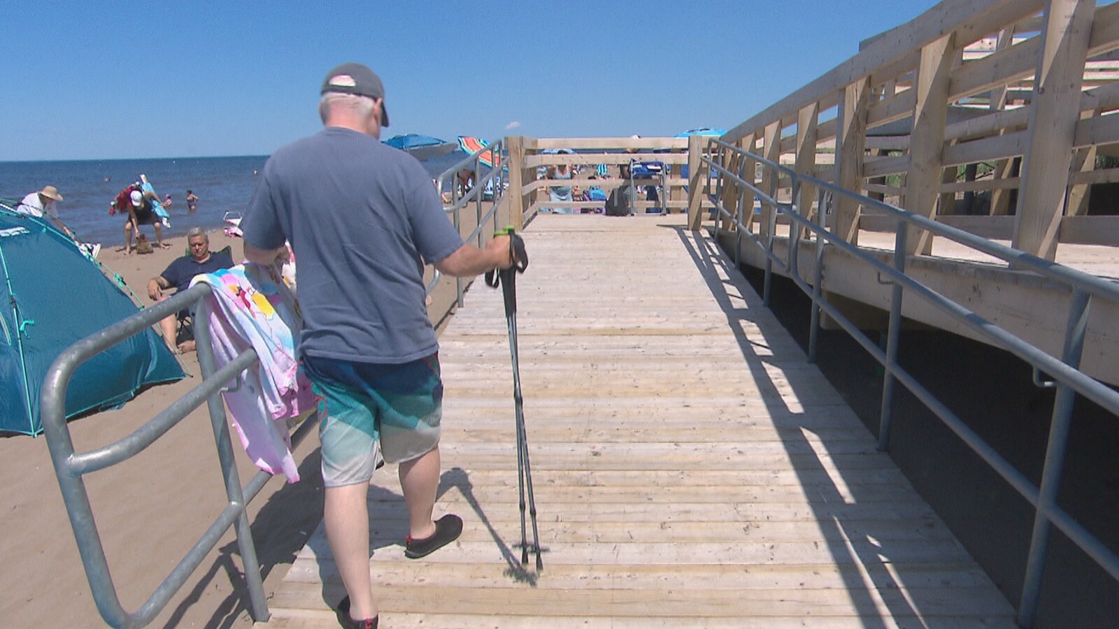 Un homme marche sur une passerelle à la plage à l'aide d'une canne.