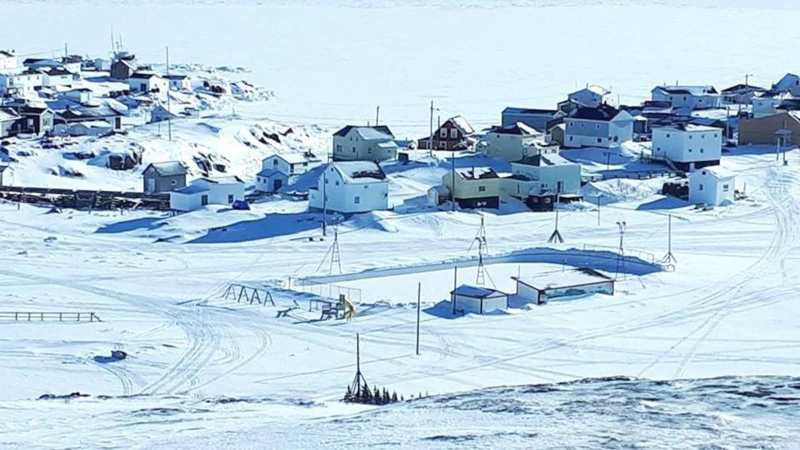 Le village de Harrington Harbour sur la Basse-Côte-Nord en février 2018 photographié d'un peu plus haut sur la rive. On peut y apercevoir la patinoire et quelques maisons et au loin le fleuve.