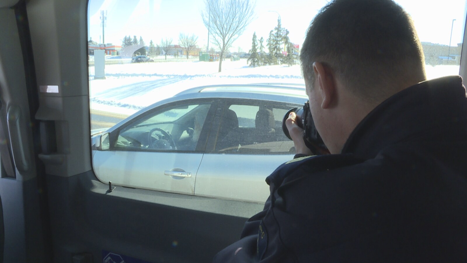 Depuis une voiture aux vitres teintées, un policier pointe sa caméra sur une automobiliste.