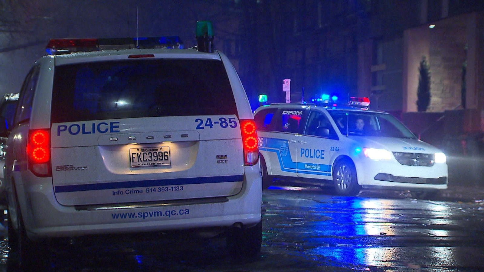 Deux fourgonnettes de policiers sont stationnées dans une rue résidentielle de Montréal en pleine nuit.