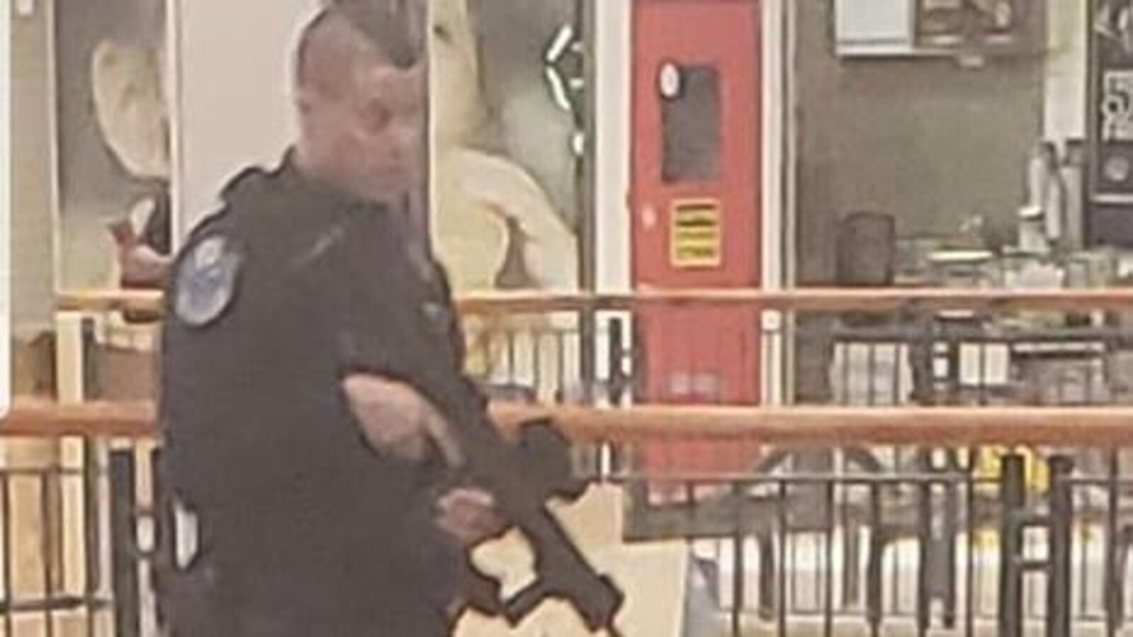 Un policier armé d'une carabine se déplaçant avec précaution dans une aire de restauration du centre commercial Avalon.