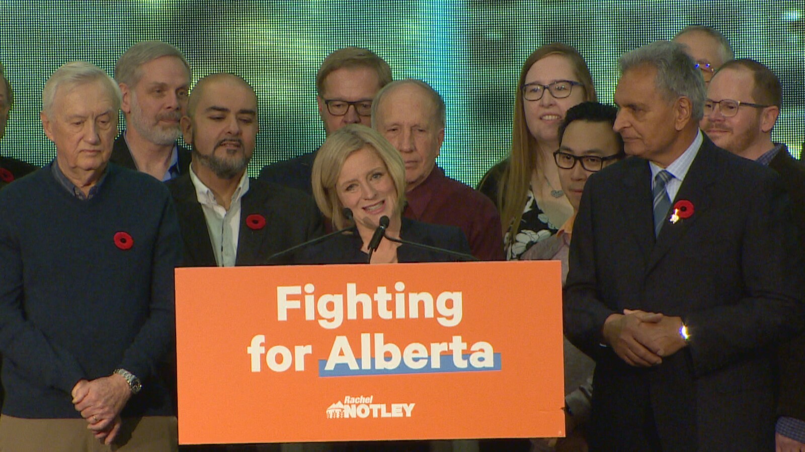 Rachel Notley s'exprime au podium, entourée des députés de son caucus.