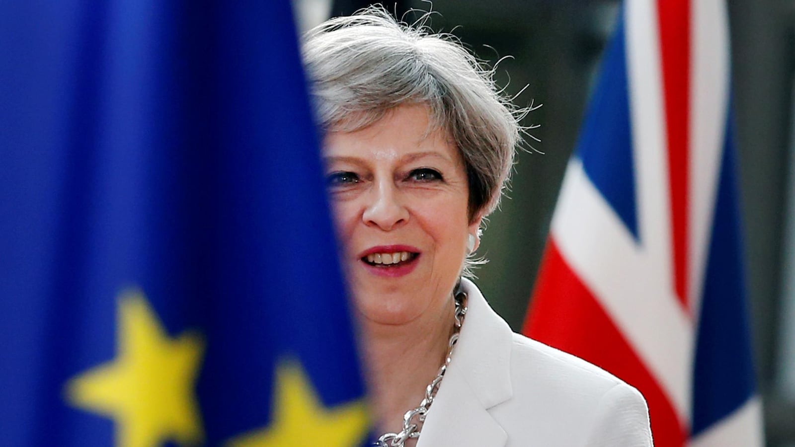 La première ministre Theresa May derrière un drapeau de l'Union européenne et devant un drapeau du Royaume-Uni.