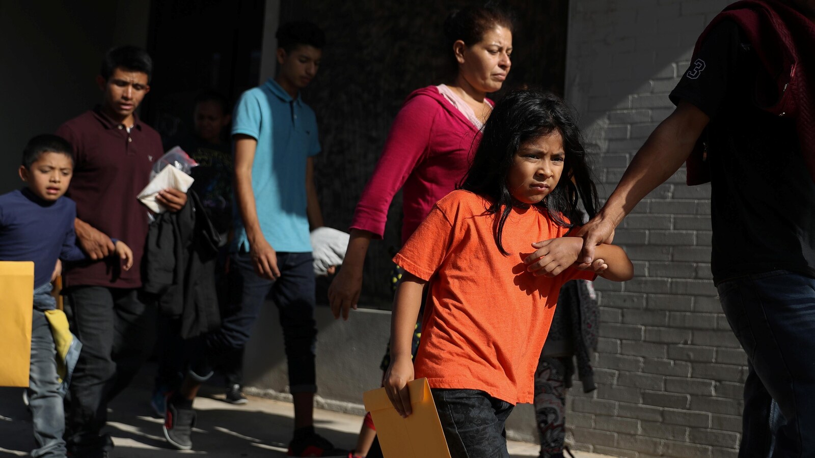Des enfants accompagnés par des adultes à l'extérieur d'un bâtiment en briques.