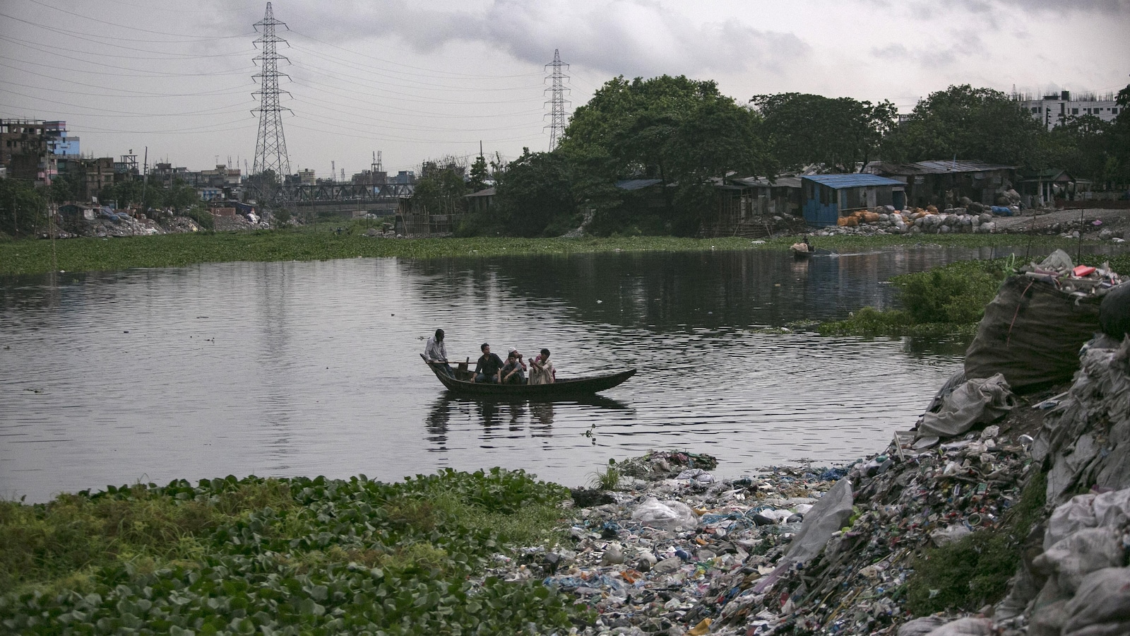 Quatre hommes naviguent en pirogue sur la rivière, dont les rives sont couvertes de déchets.