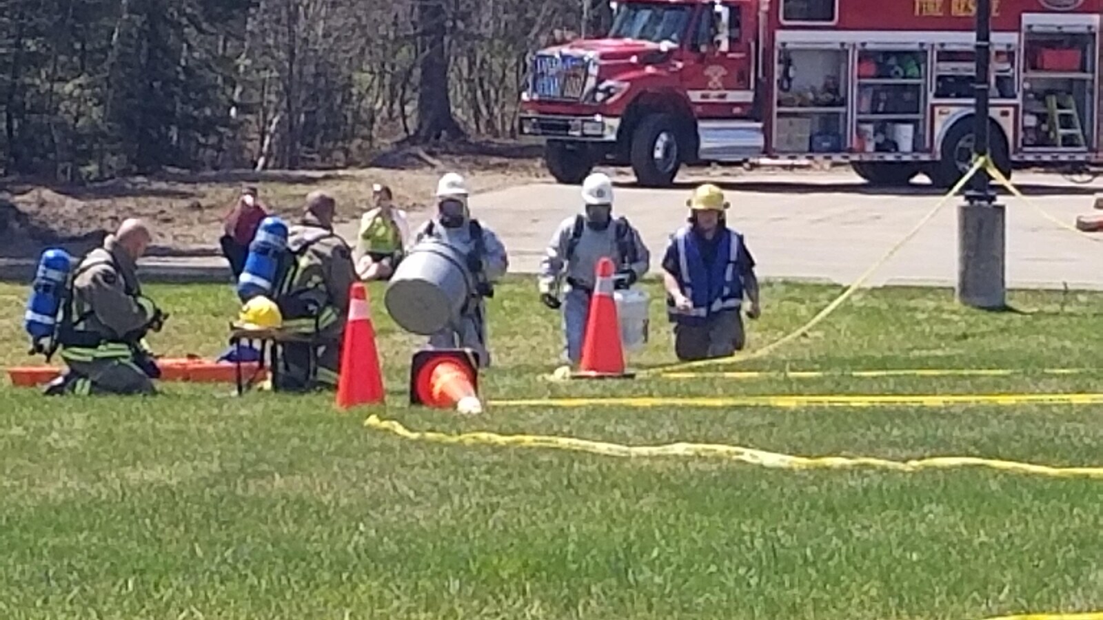 Des pompiers dans le gazon entourés de cônes et devant un camion de pompiers.