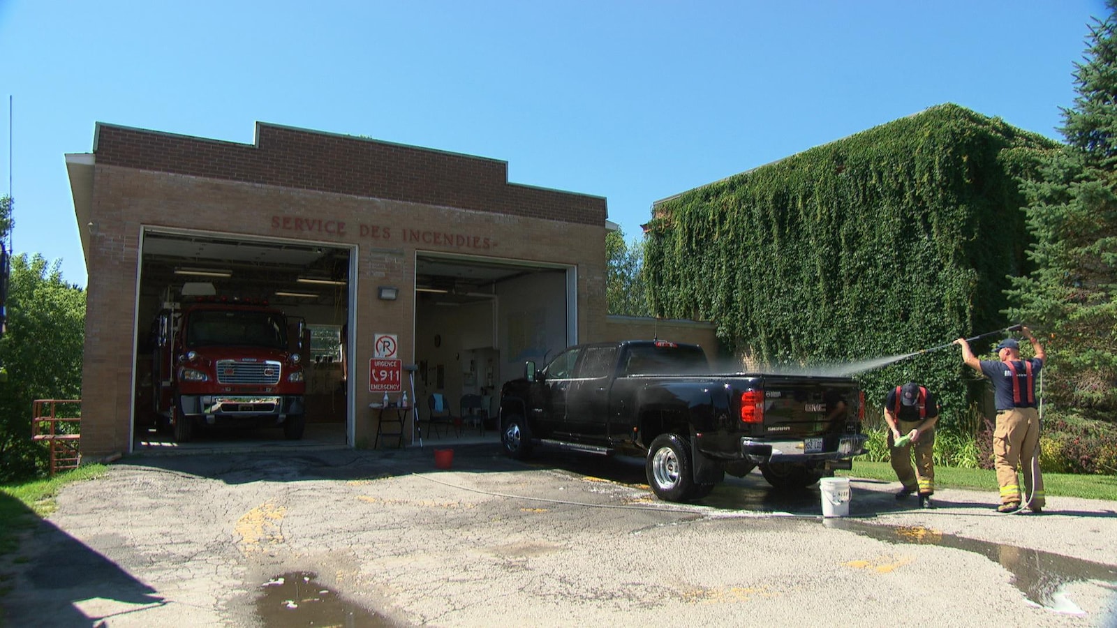 Deux pompiers lavent une camionnette devant une caserne de pompiers.