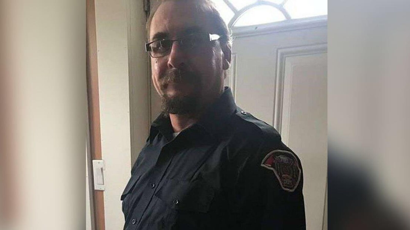 Portrait d'un homme avec une barbe dans l'entrée d'une maison portant l'uniforme de pompier.