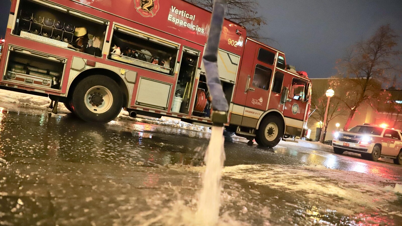 Un camion de pompier avec un tuyau qui déverse de l'eau en premier plan.