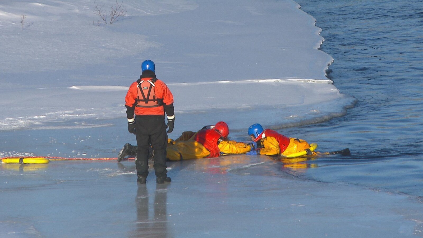 Deux pompiers couchés sur la glace tirent un troisième pompier qui fait la victime.