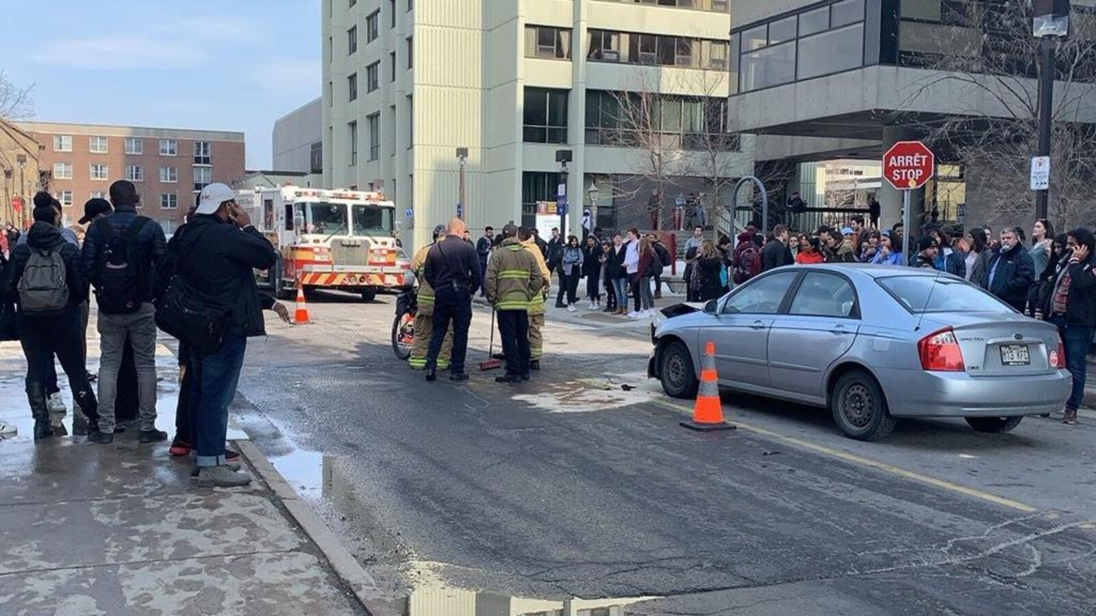 Des pompiers nettoient la chaussée avec un balai. Le devant d'une voiture est endommagé.