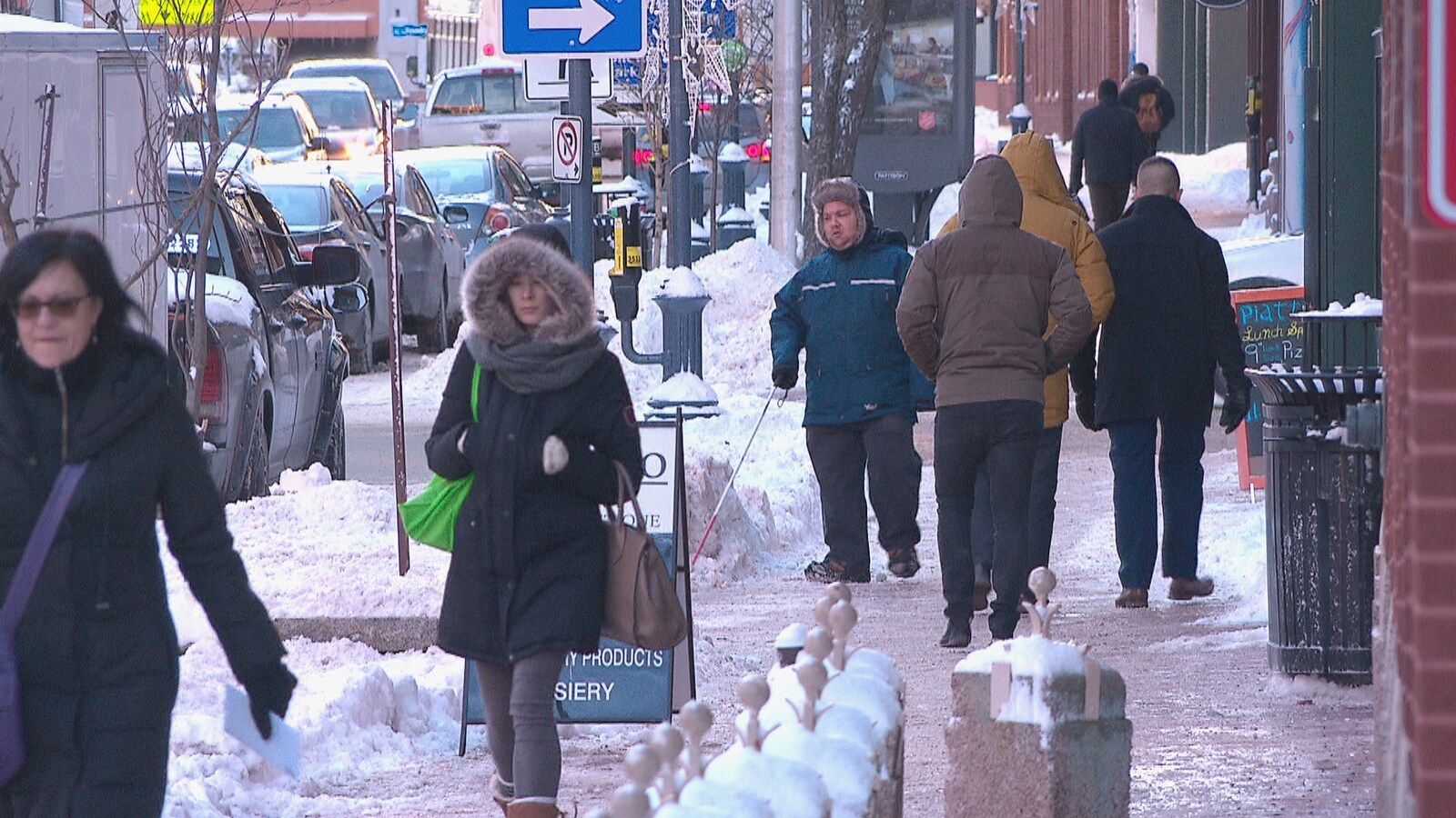 En hiver, différentes personnes marchent sur un trottoir de Moncton.