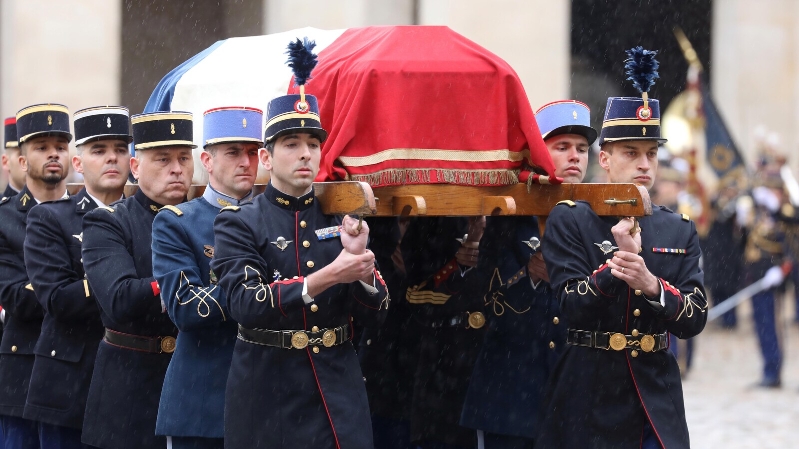 Des gendarmes portent un cercueil.