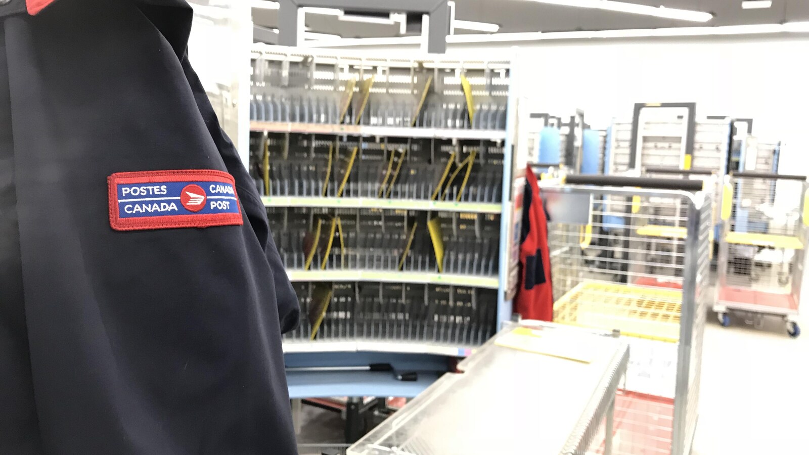 Un manteau de facteur en premier plan, un centre de distribution en arrière-plan.