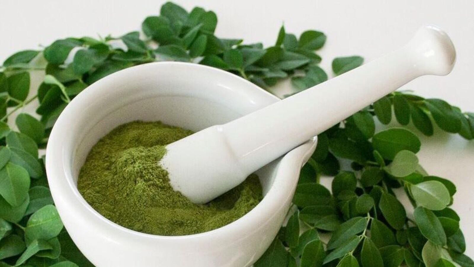 De la poudre verte dans un bol entouré de feuilles de moringa.