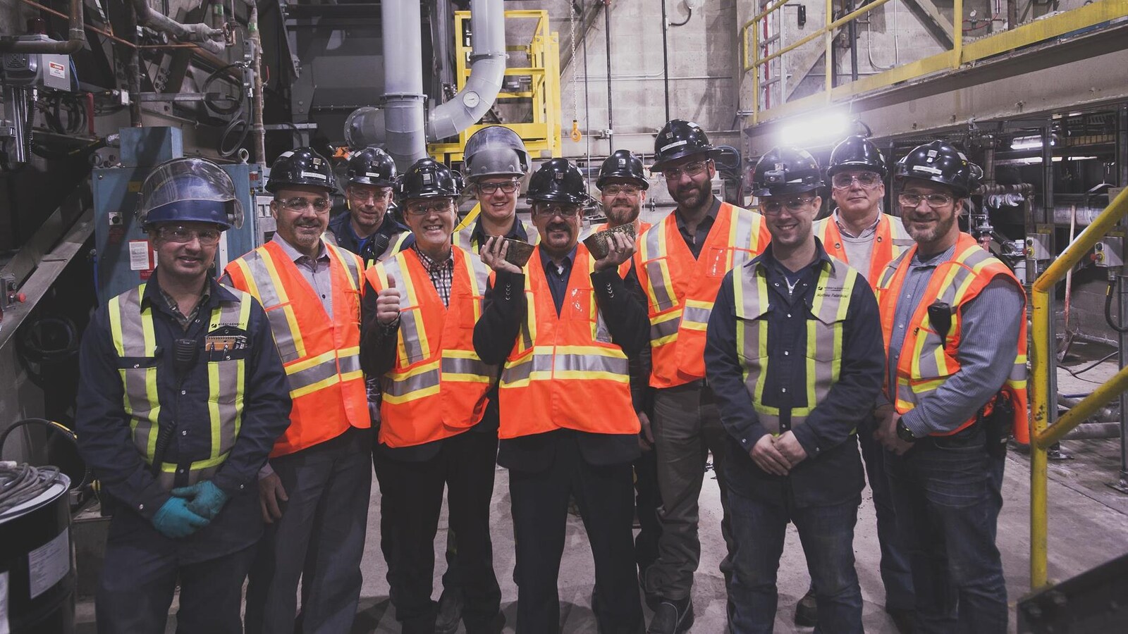Une équipe de mineurs pose avec deux lingots d'or, dans une usine.
