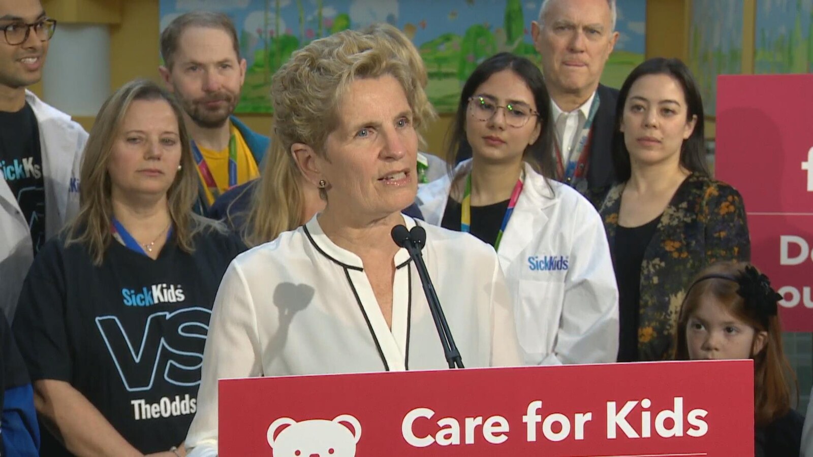 Photo de Kathleen Wynne portant une blouse blanche au podium.