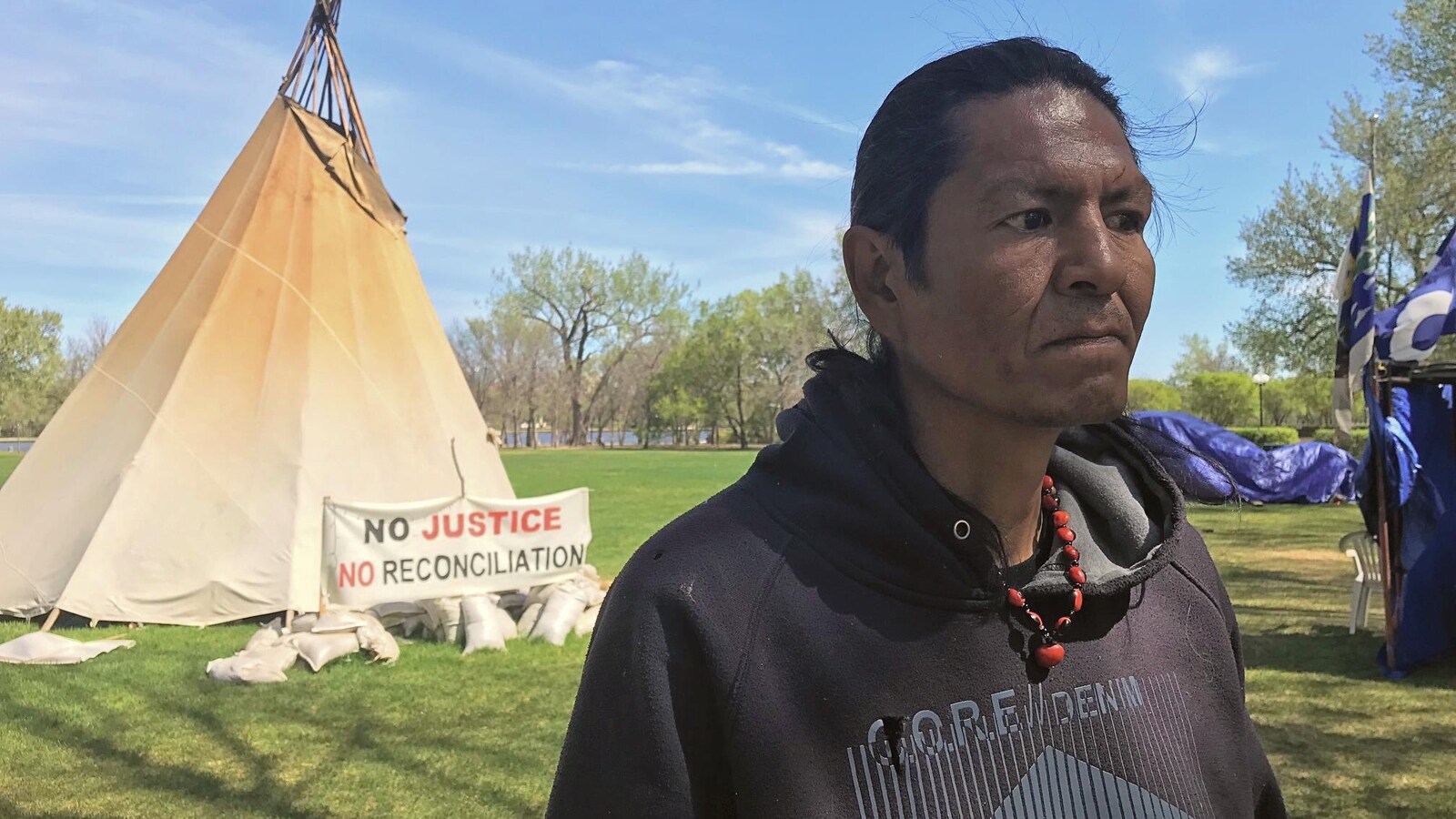 Le manifestant Prescott Demas se tient debout devant un tipi planté devant l'Assemblée législative à Regina