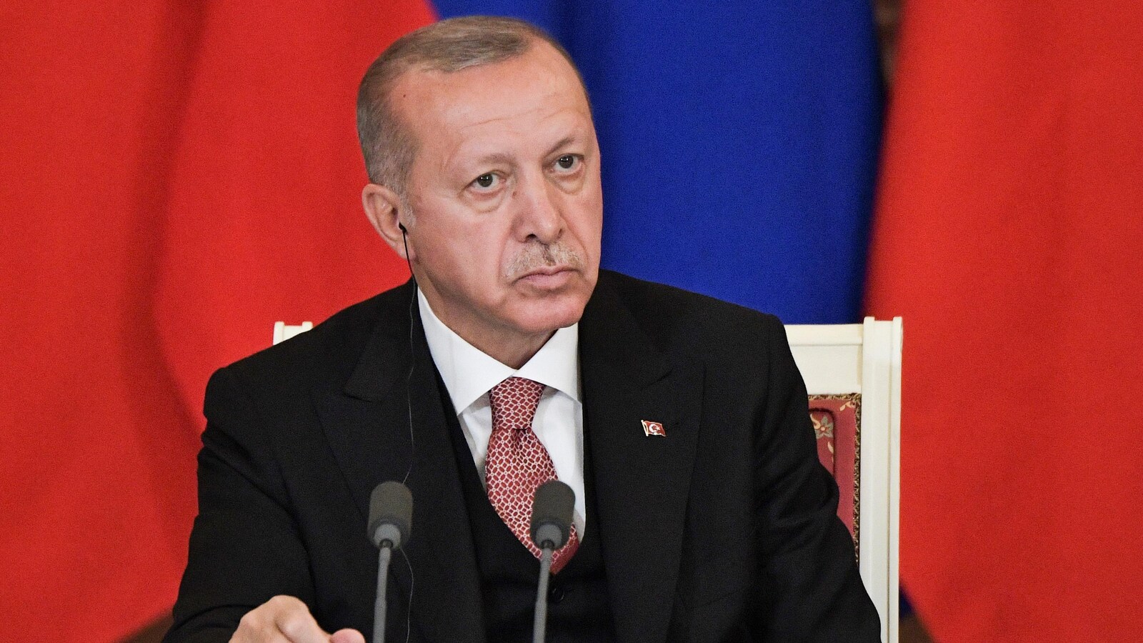 Le président turc Recep Tayyip Erdogan est assis sur une chaise devant deux micros.