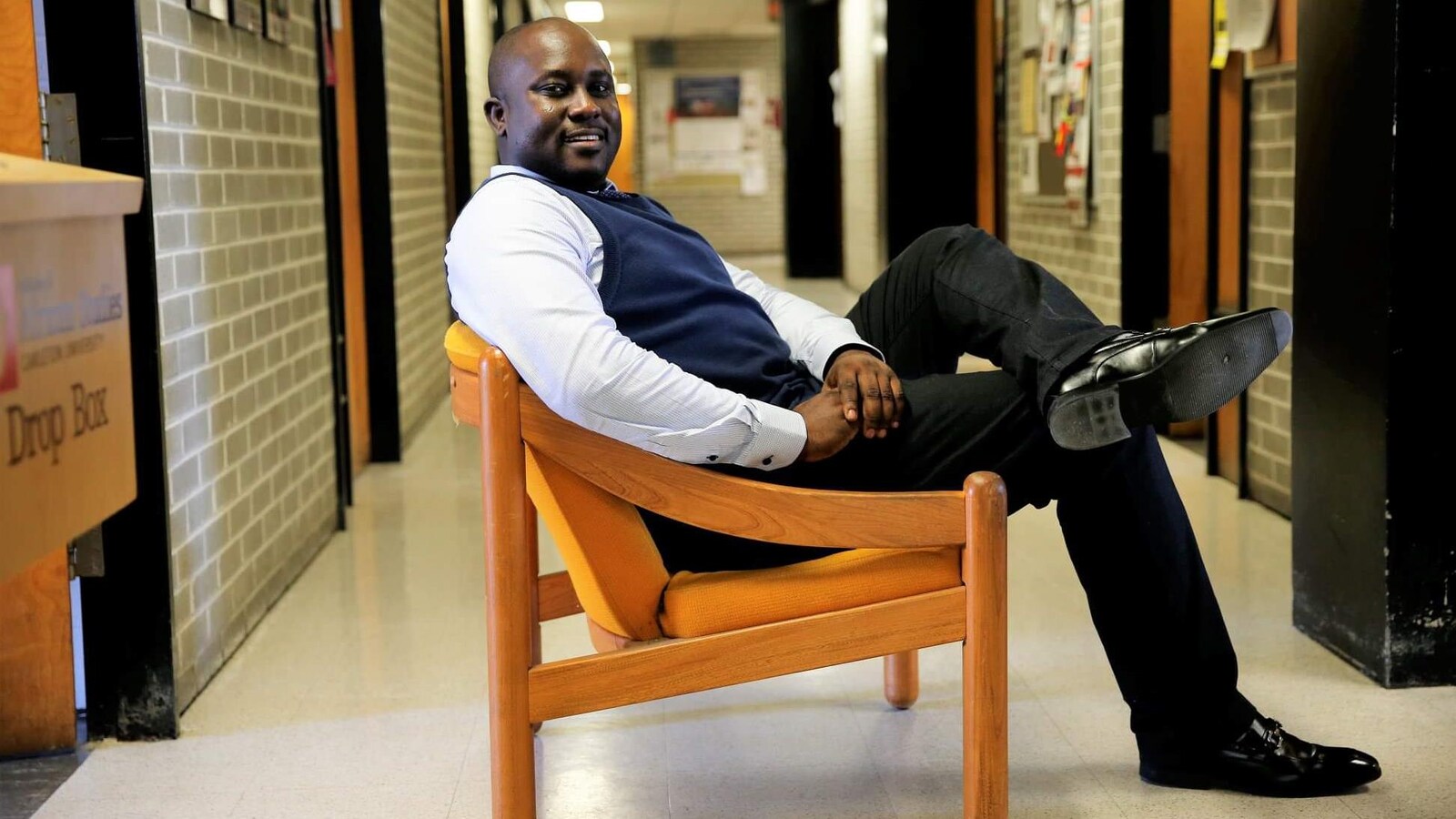 Pius Adesanmi est assis sur une chaise dans un corridor d'université.