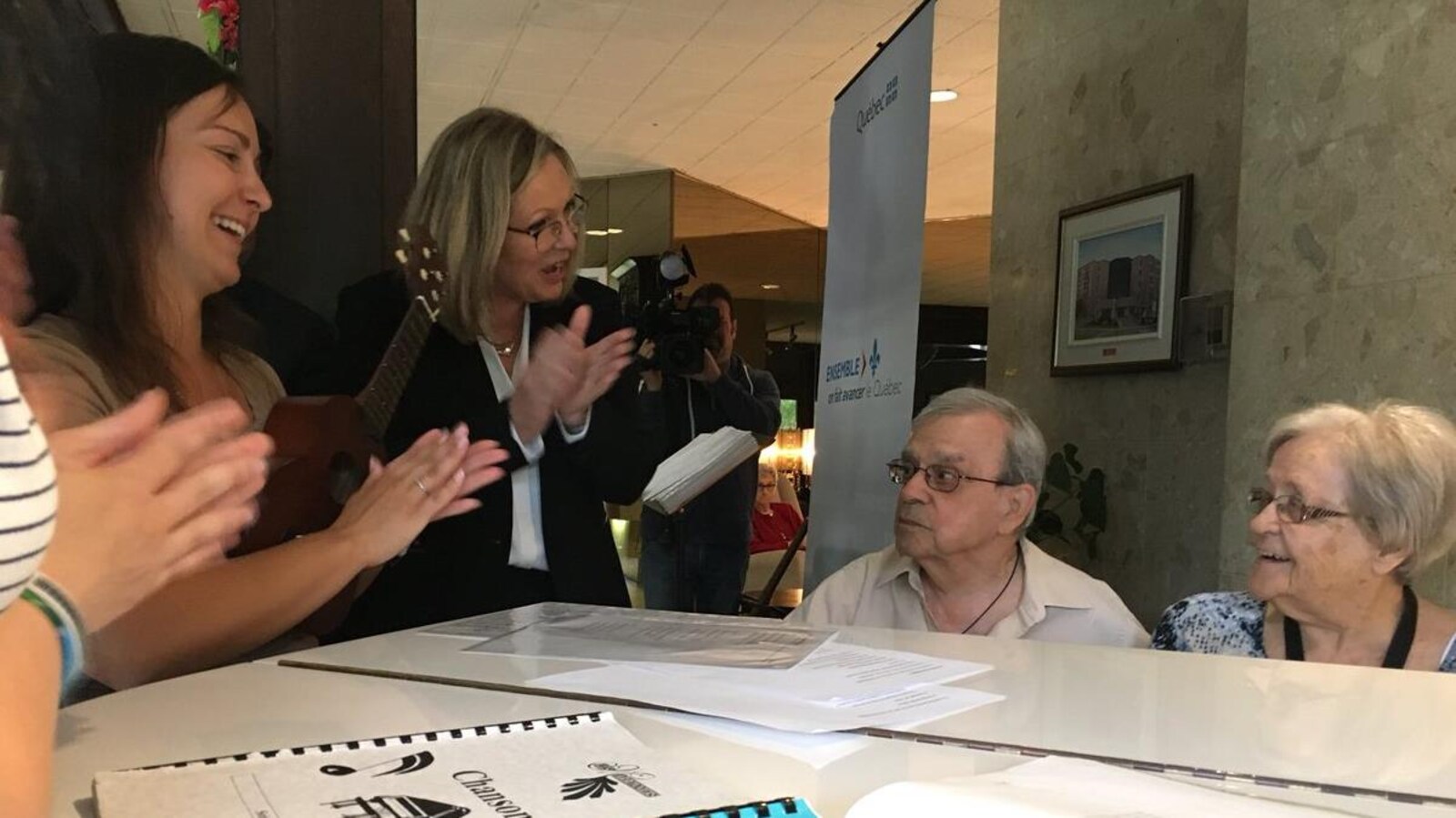 La ministre responsable des Aînés, Francine Charbonneau et Joliane Plante chantent autour d'un piano avec des résidents de la Résidence Les Marronniers.