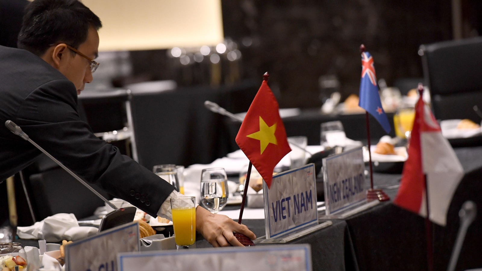 Un homme débarrasse une table sur laquelle est placée de la nourriture ainsi que des petits drapeaux identifiant le pays d'origine des participants à une rencontre des pays du littoral du Pacifique.