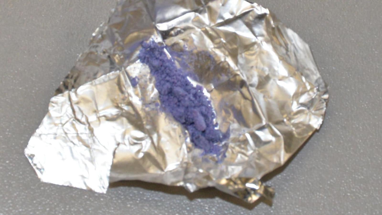 Une poudre violette déborde d’un sachet d'héroïne entrouvert.