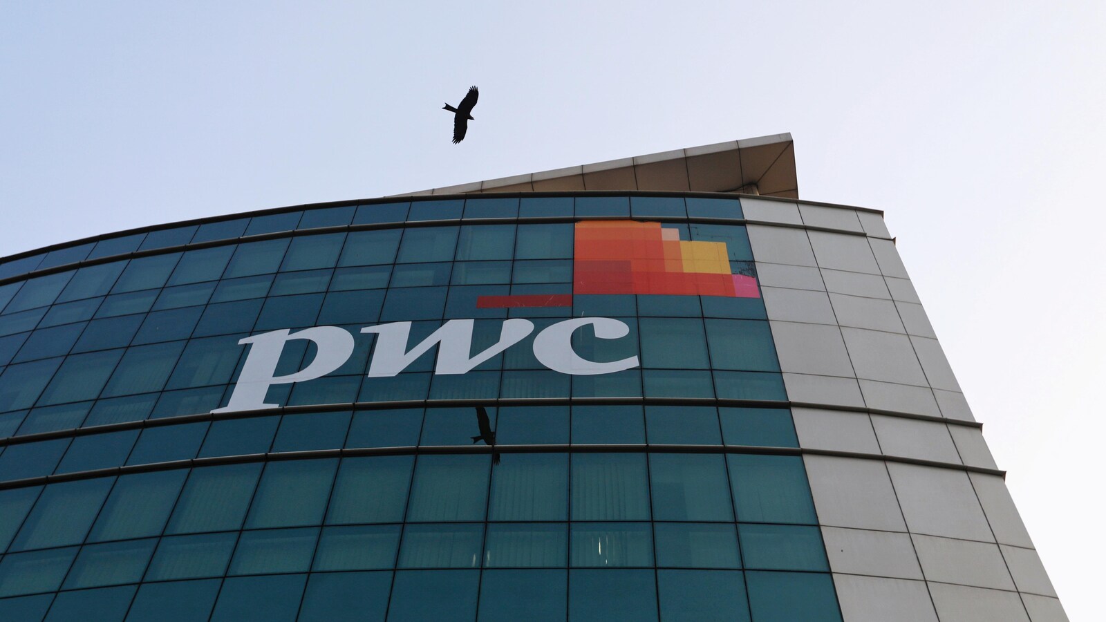 Un oiseau passe devant le logo de Price Waterhouse installé sur la façade de son bureau à Mumbai.