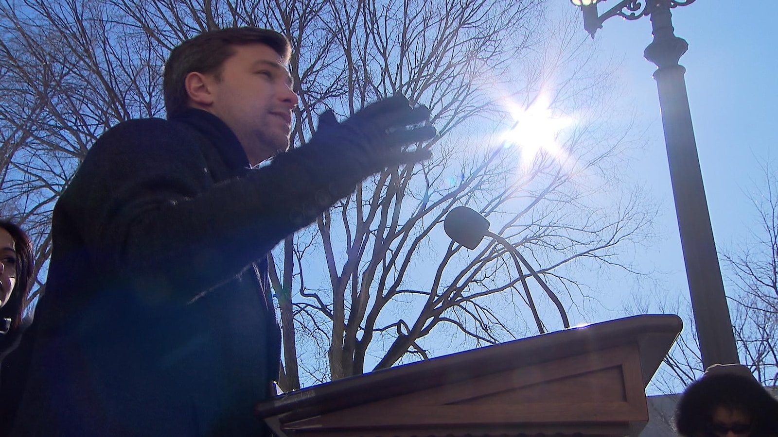Gabriel Nadeau-Dubois parle derrière un podium placé à l'extérieur. On voit des arbres en arrière-plan.