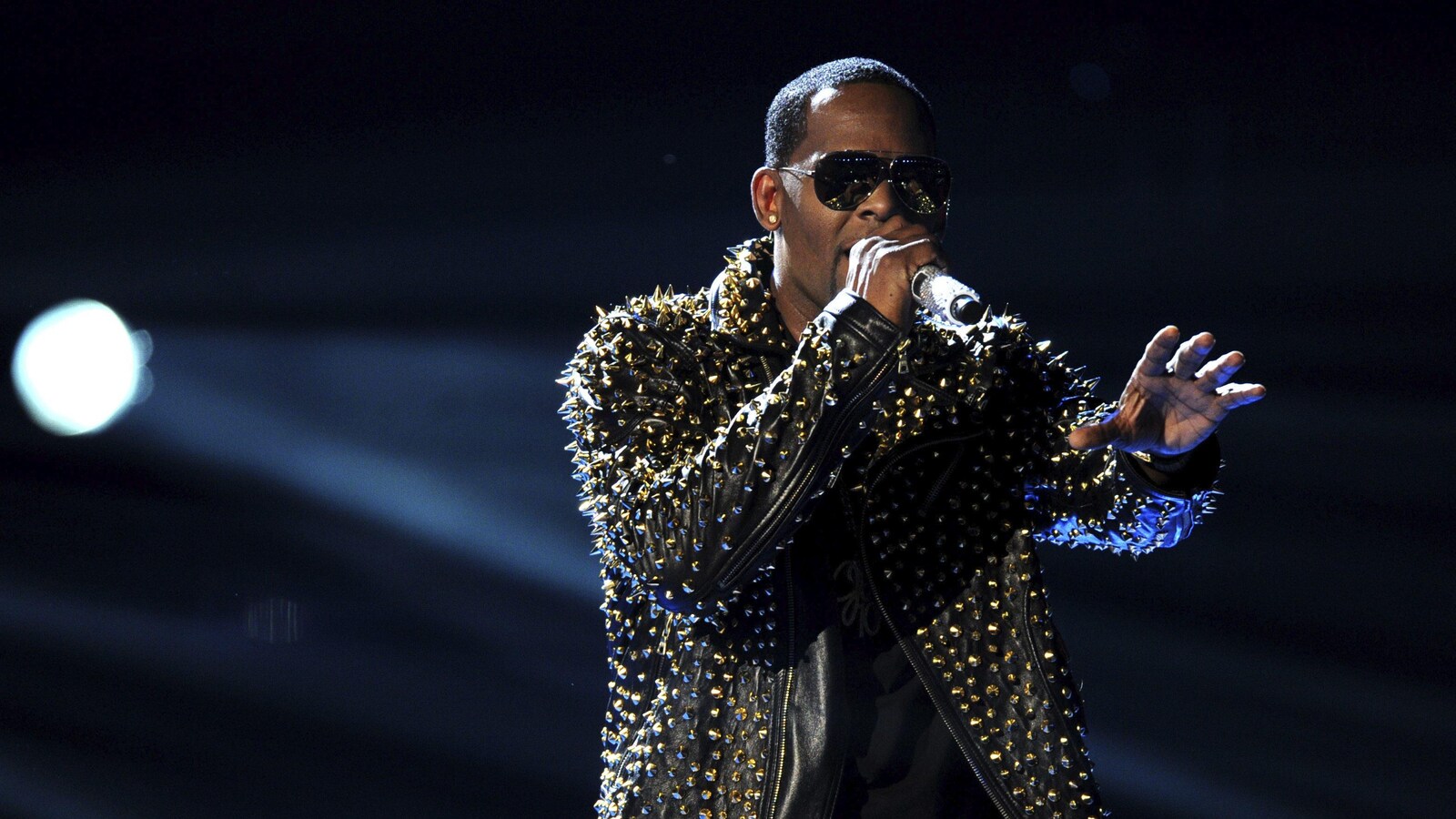 Le chanteur R. Kelly donne un spectacle sur un scène, un micro à la main.