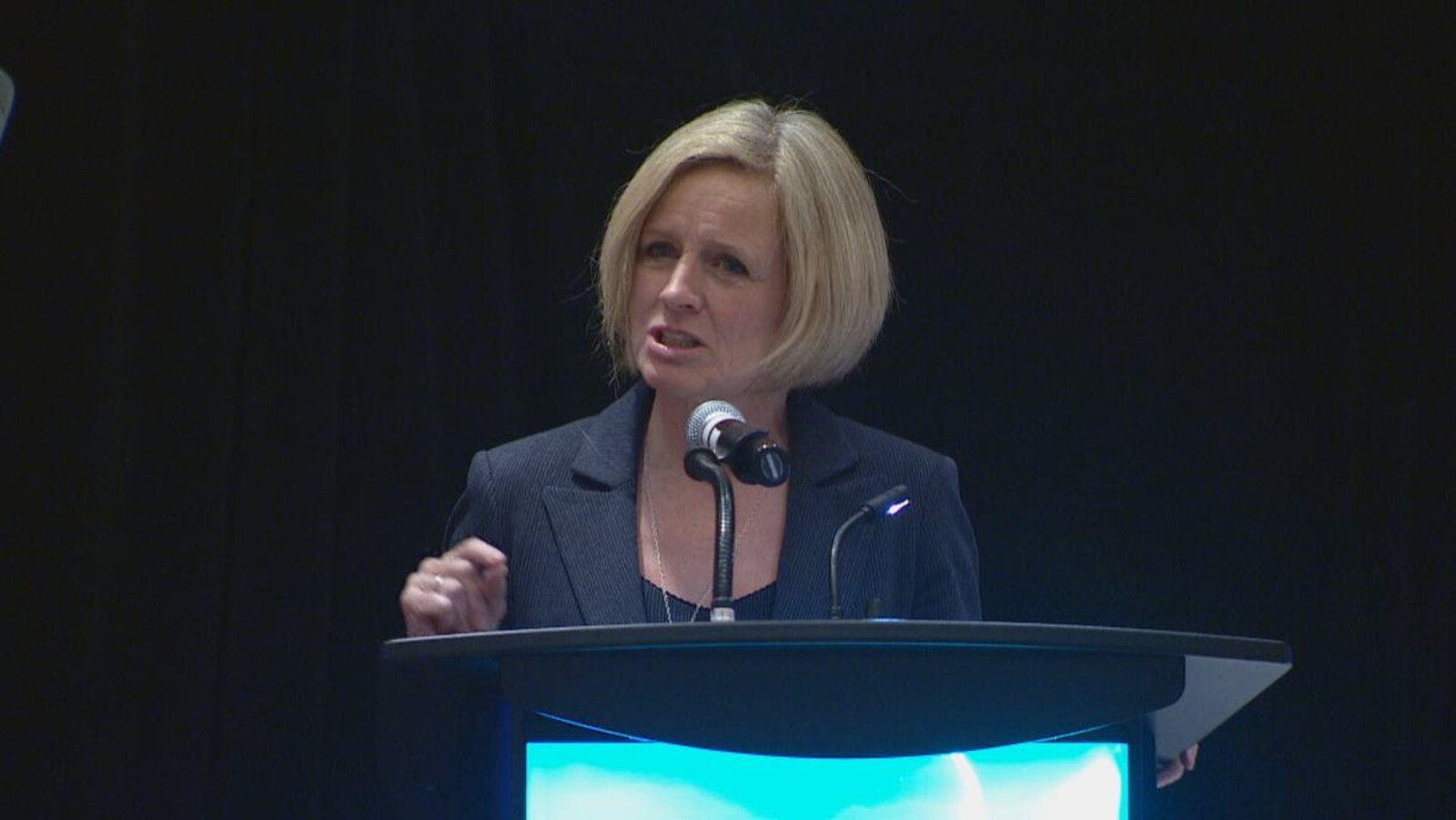 Rachel Notley, derrière un lutrin, face à un micro.