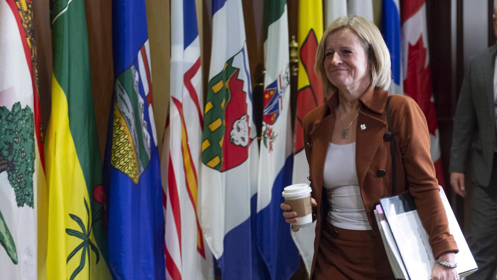 La première ministre de l'Alberta, Rachel Notley, marche devant une rangée de drapeaux des provinces et des territoires.