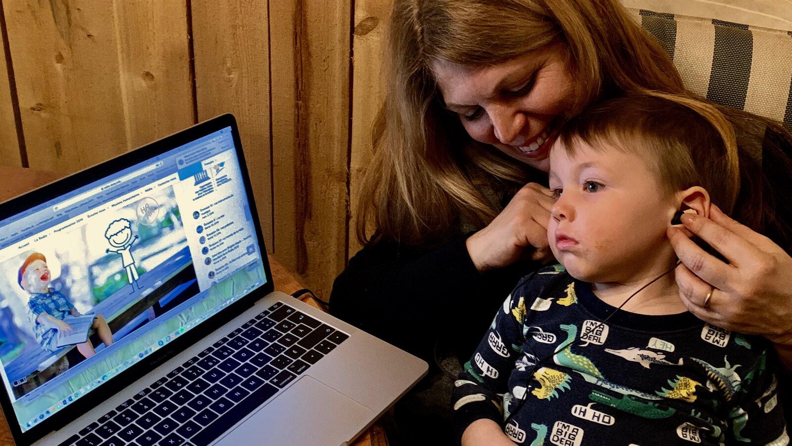 Un enfant en pyjama sur les genoux de sa mère qui écoute la radio avec des écouteurs.