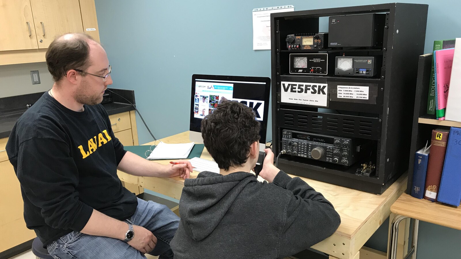 Un jeune tient un microphone dans sa main, à côté de son professeur.
