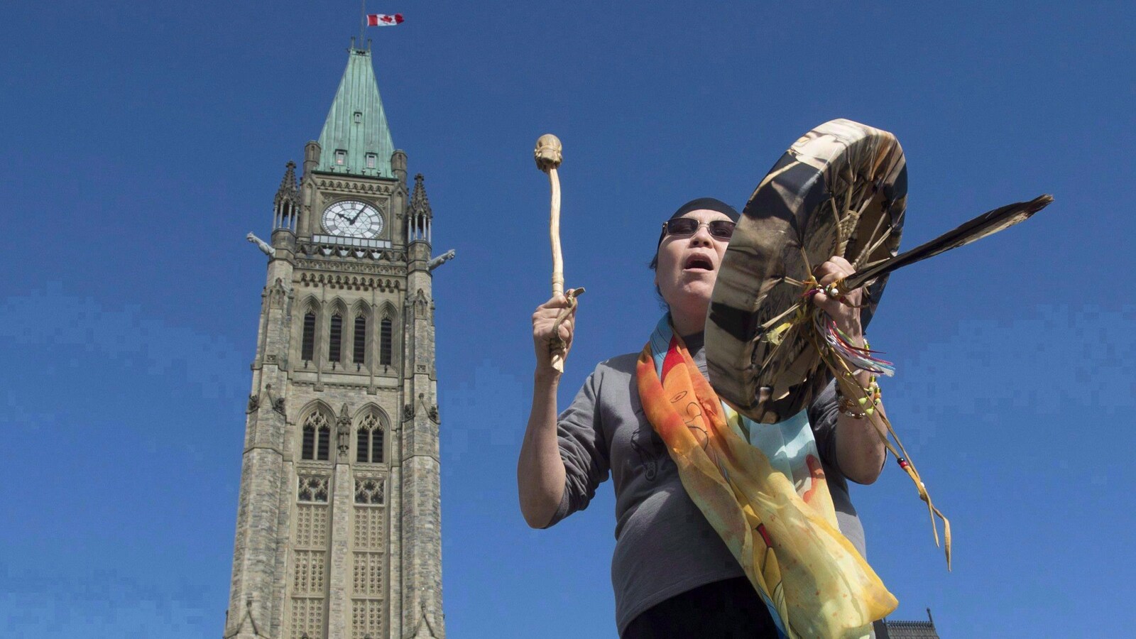 Une femme autochtone joue du tambourin devant l'édifice du Parlement à Ottawa.