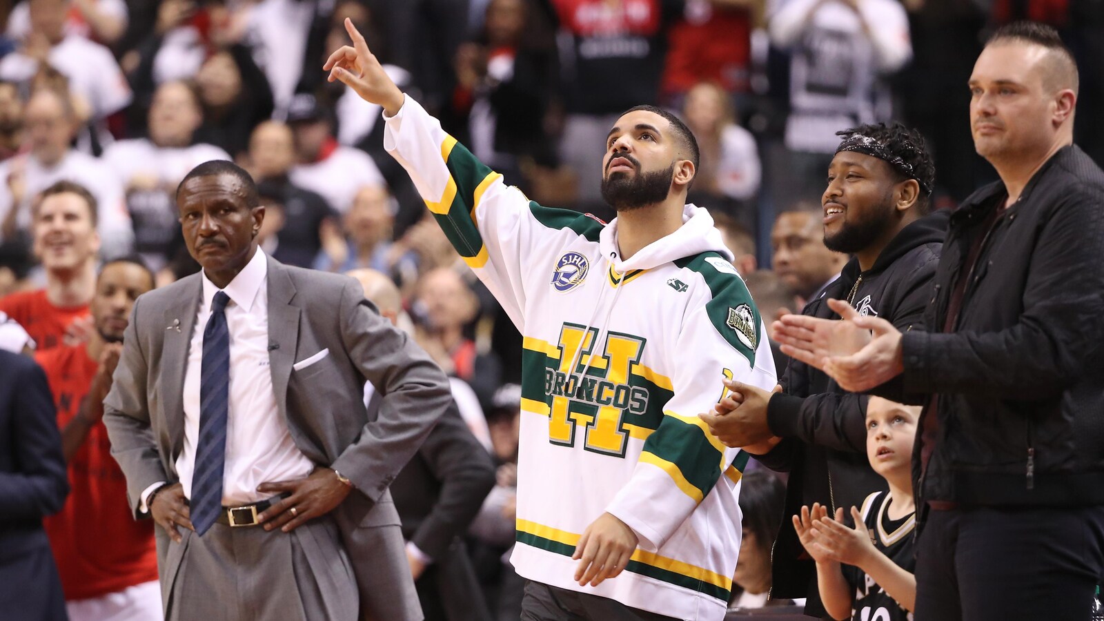 Le rappeur Drake est debout, au milieu de gens, et porte un maillot aux couleurs des Broncos de Humboldt. Il pointe vers le ciel.