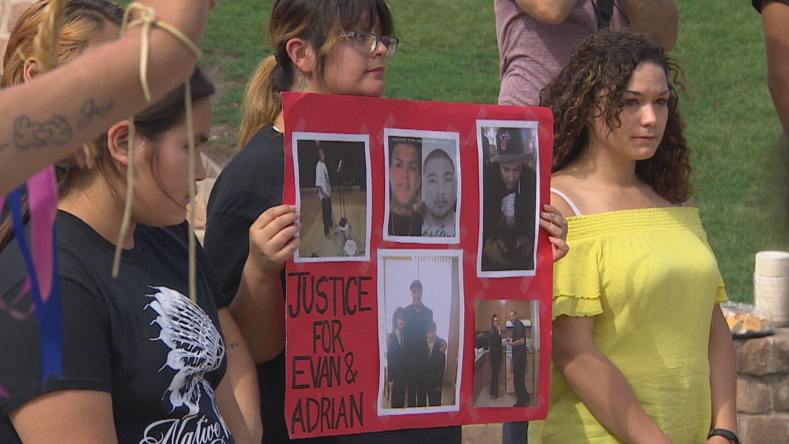 Une femme au sein d'une foule tient une pancarte demandant justice pour la mort de deux hommes.