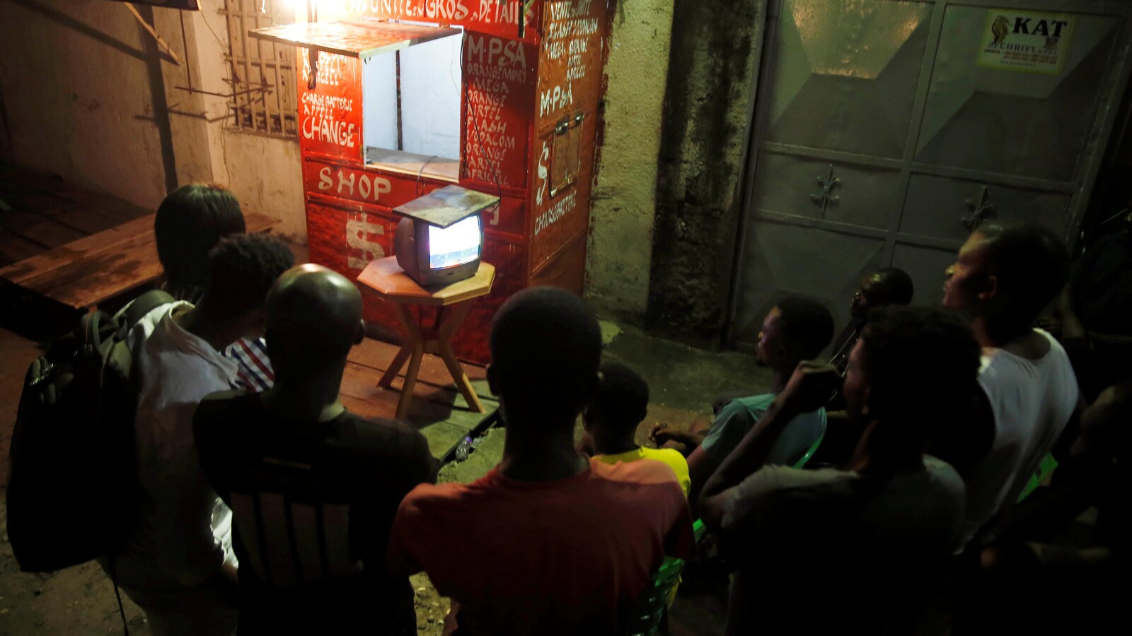 Des gens sont devant une petite télévision posée sur une table.
