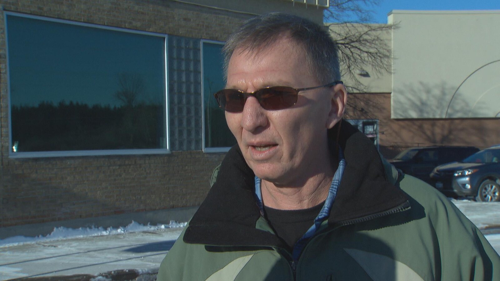 Réal Backaund répond aux questions d'une journaliste, dehors, devant un bâtiment, en hiver.