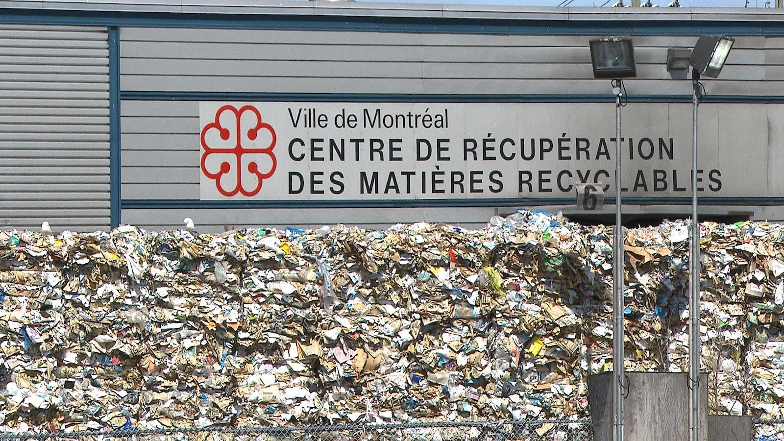 Une montagne de débris devant le mur du bâtiment sur lequel il est écrit: «Ville de Montréal, Centre de récupération des matières recyclables» avec le logo de la Ville de Montréal.
