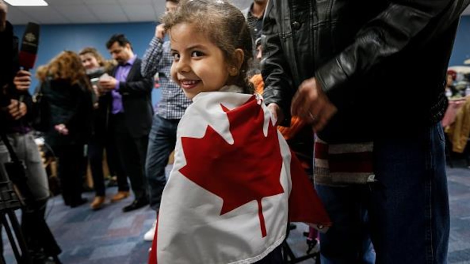 Une petite fille souriante est enveloppée dans un drapeau canadien lors d'un point de presse.