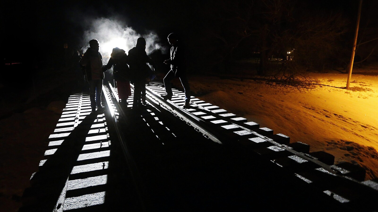Des demandeurs d'asile marchent sur voie ferrée, dans la noirceur.