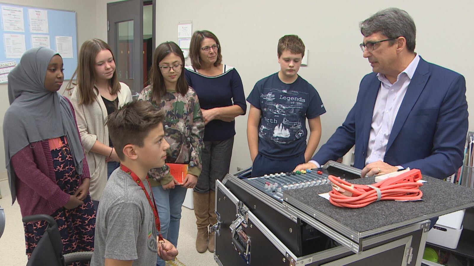 Autour d'une grande boîte noire comportant un clavier de boutons sur le dessus, sont rassemblés cinq jeunes élèves et deux adultes.