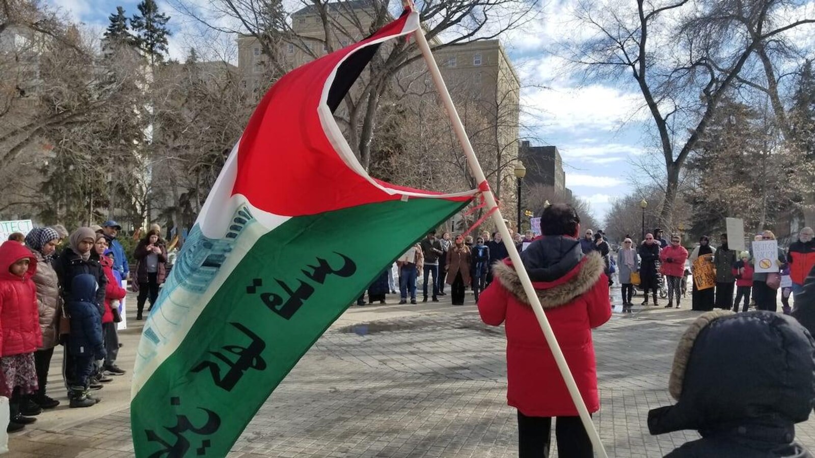 Des dizaines de personnes forment un cercle et brandissent des pancartes sur une place à Regina en hommage aux victimes de l'attentat en Nouvelle-Zélande.