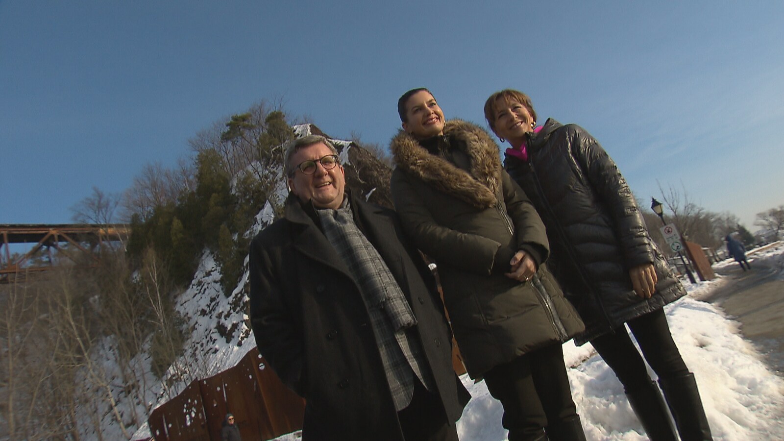 Photographie en contreplongée de Régis Labeaume, Geneviève Guilbault et Nathalie Roy prise en hiver. On aperçoit, à l’arrière-plan, le tracel et la falaise de Cap-Rouge.