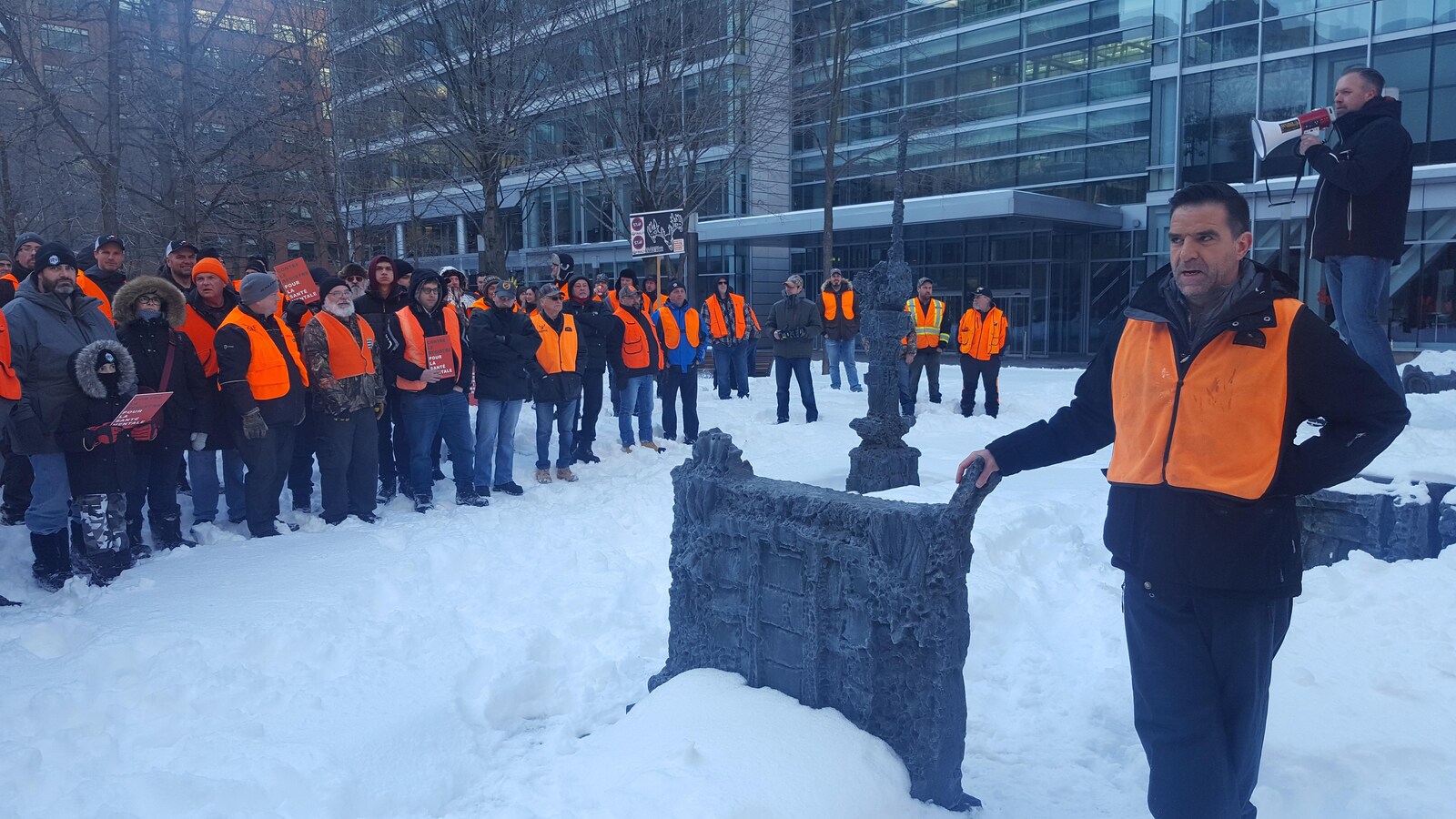 Des personnes portant des gilets oranges et des manteaux d'hiver se tiennent debout dans un parc au centre-ville de Montréal.