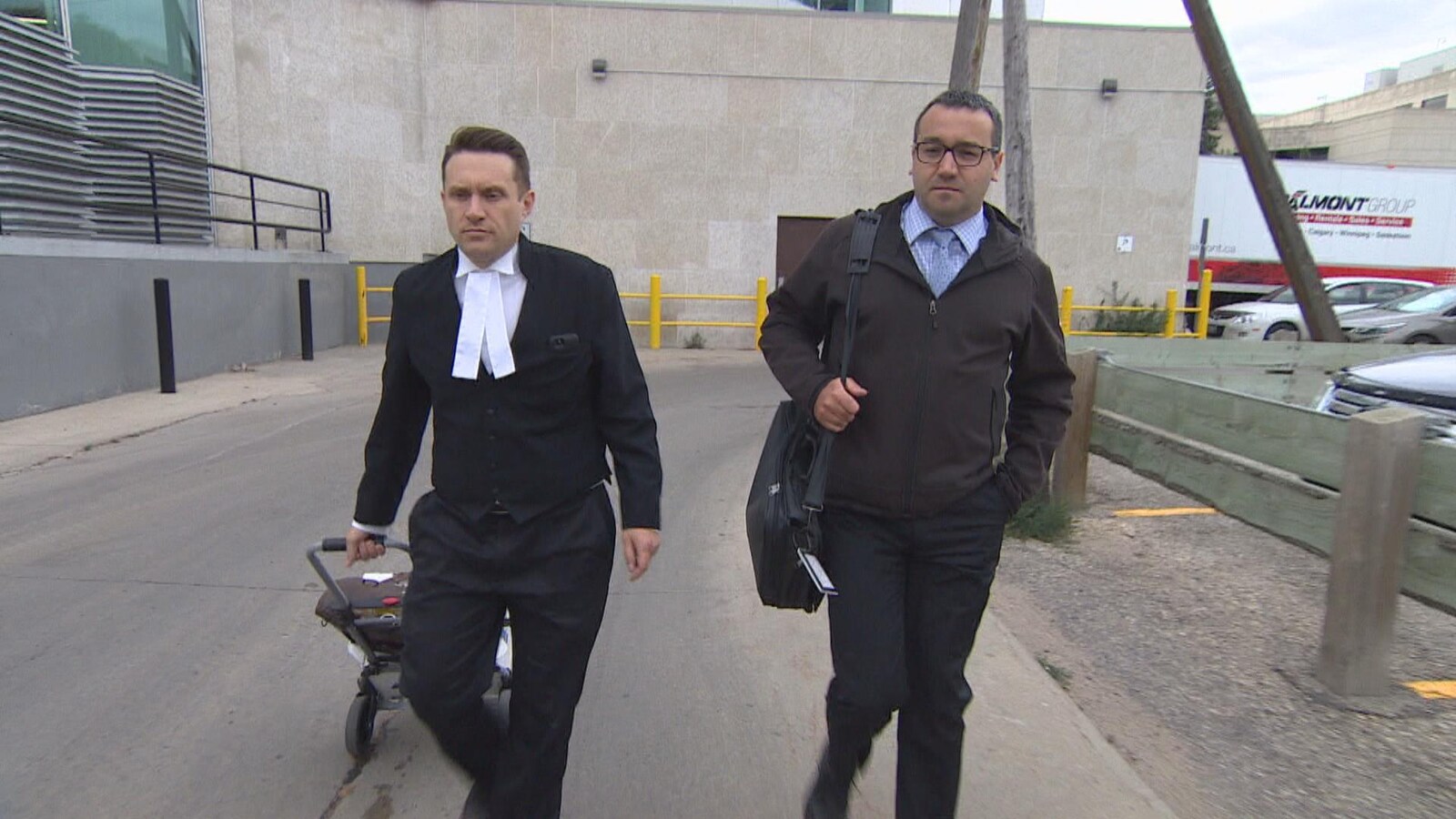 Deux hommes vêtus de noir marchent à l'extérieur.