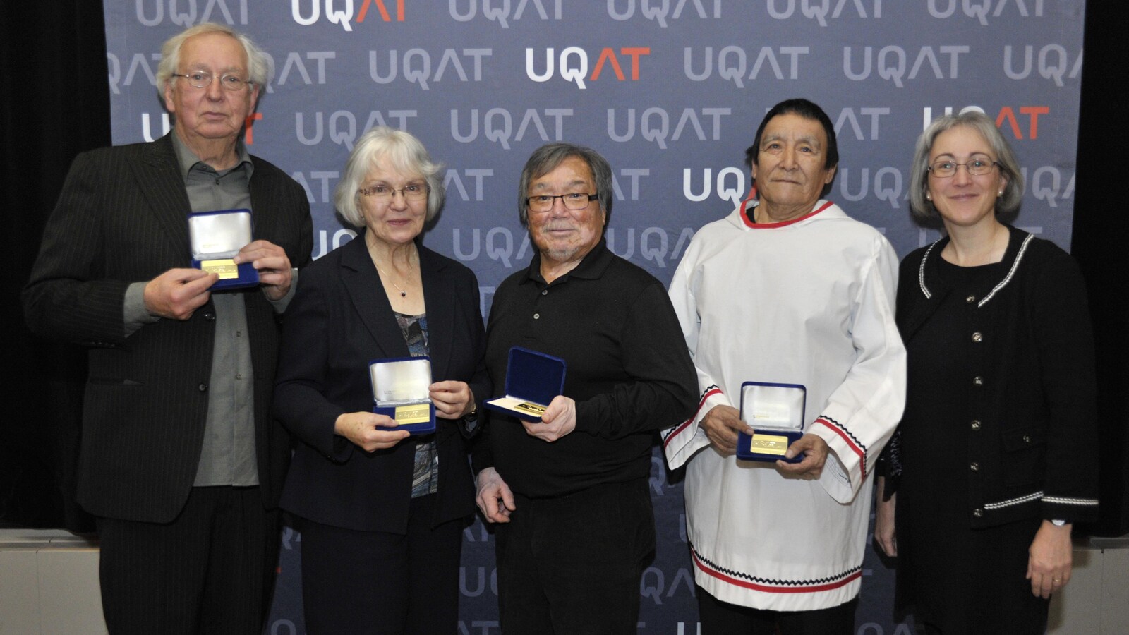 Quatre personnes tiennent des coffrets contenant une médaille honorifique devant une bannière de l'UQAT.