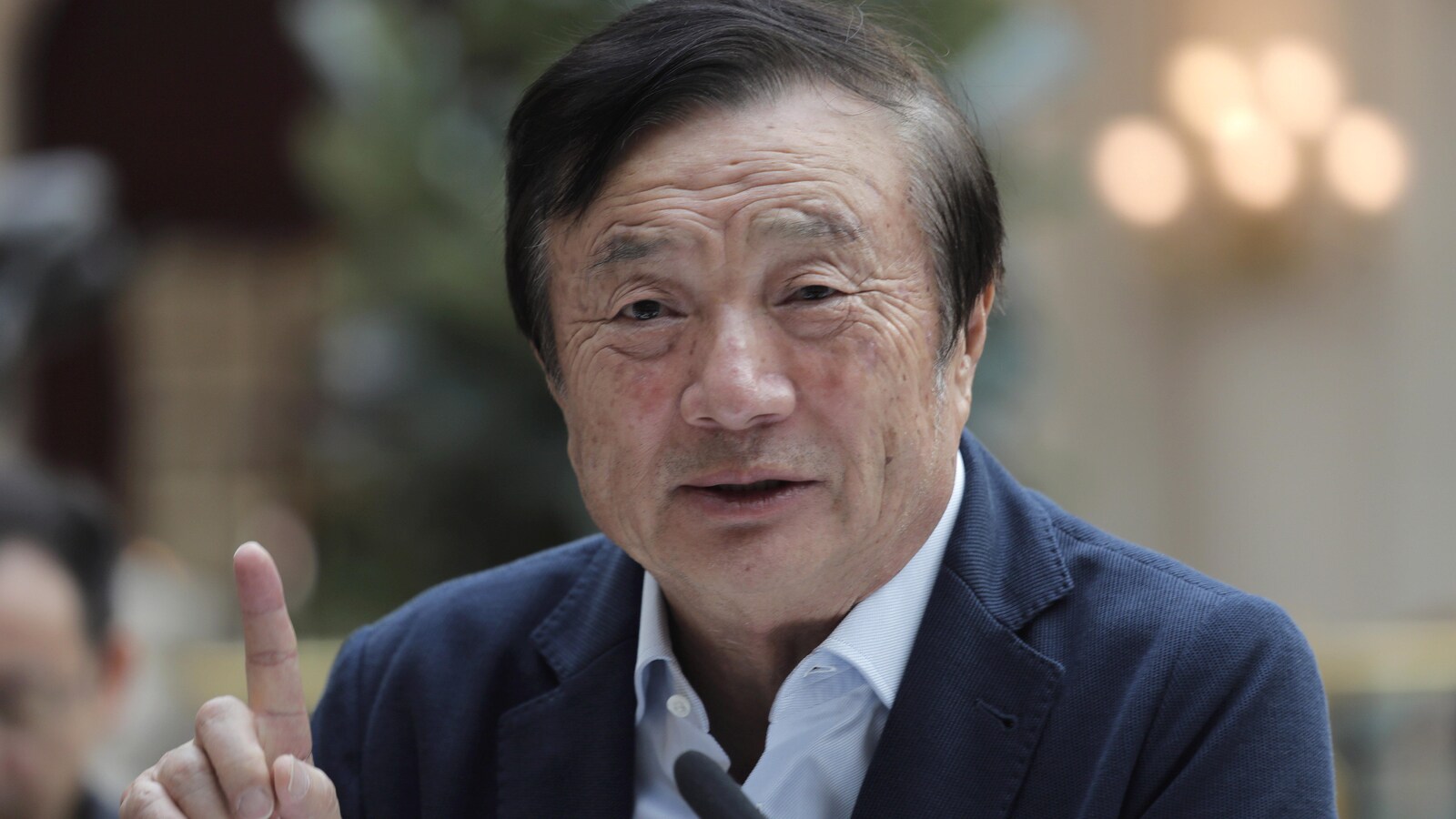Un homme asiatique lève l'index et parle dans un micro.